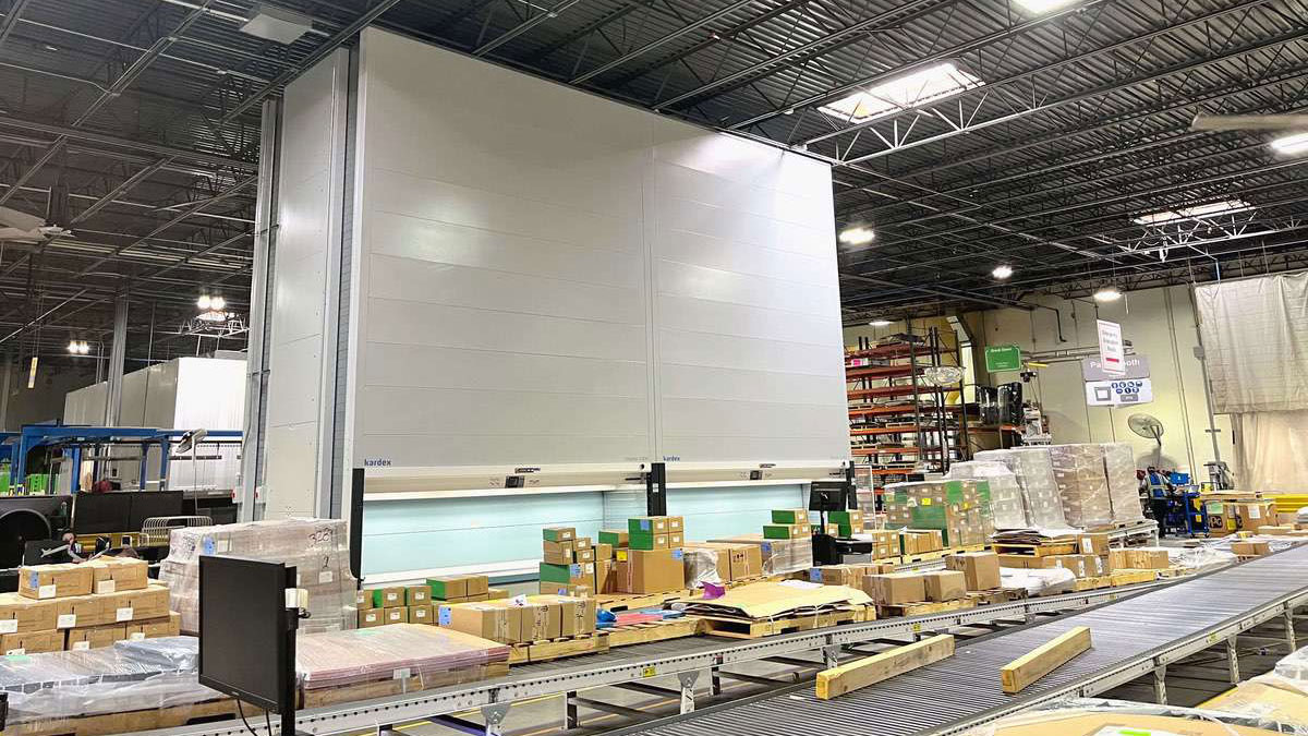 Kardex Remstar automated storage and retrieval system operating in a busy warehouse with conveyor integration for rapid item handling