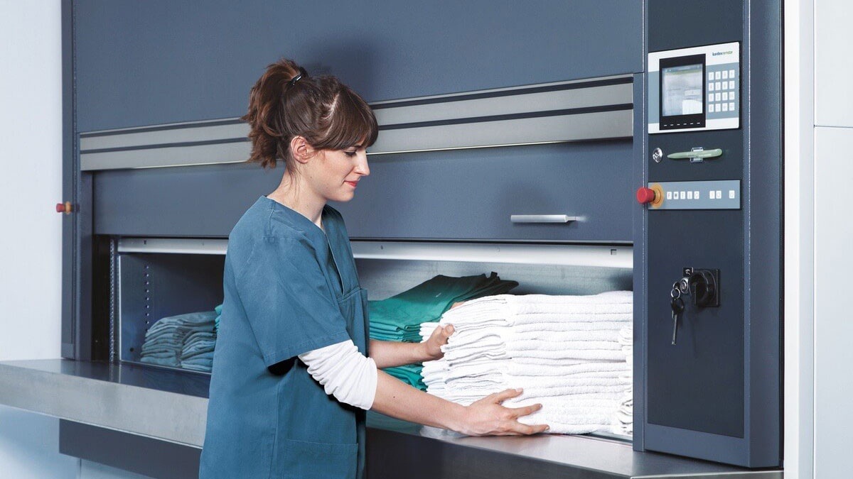 Medical worker placing clean linens into a Kardex Megamat vertical carousel, showcasing automated linen storage in clinical environments