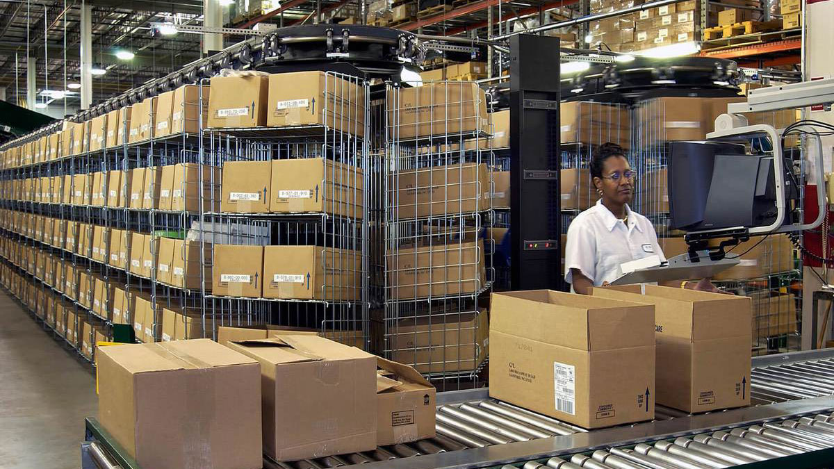Warehouse worker using an integrated touchscreen control panel to operate a horizontal carousel storage system for efficient space-saving inventory management.