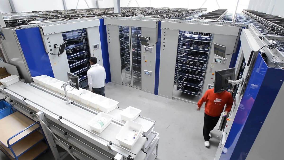 Extensive horizontal carousel system layout in a distribution center, showcasing overhead conveyor integration and streamlined picking workflows