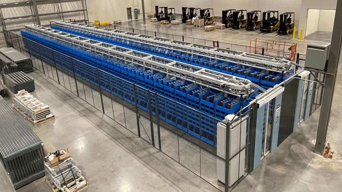 Operator working with a computer terminal at a warehouse station with multiple horizontal carousels storing high-volume packaged goods in labeled bins.