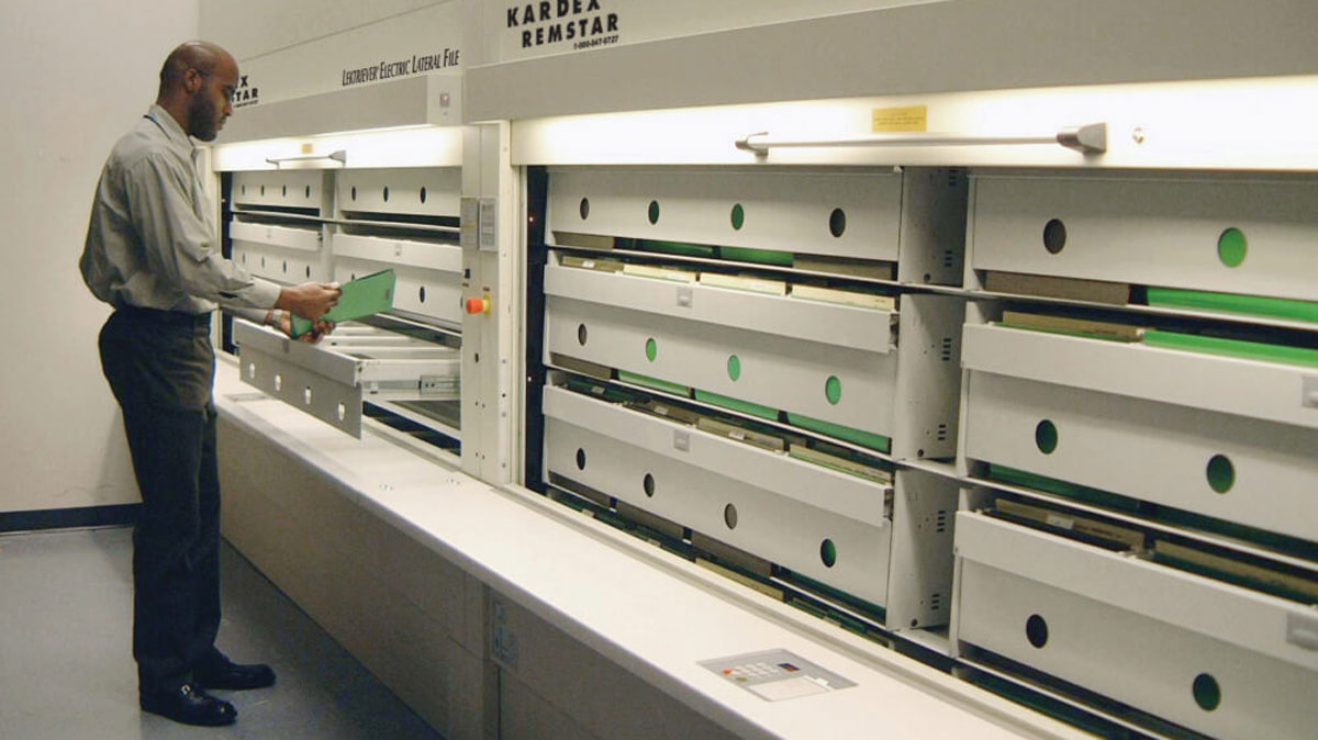 Office worker accessing medical records in an electric carousel filing system featuring multiple drawers and ergonomic workspace integration