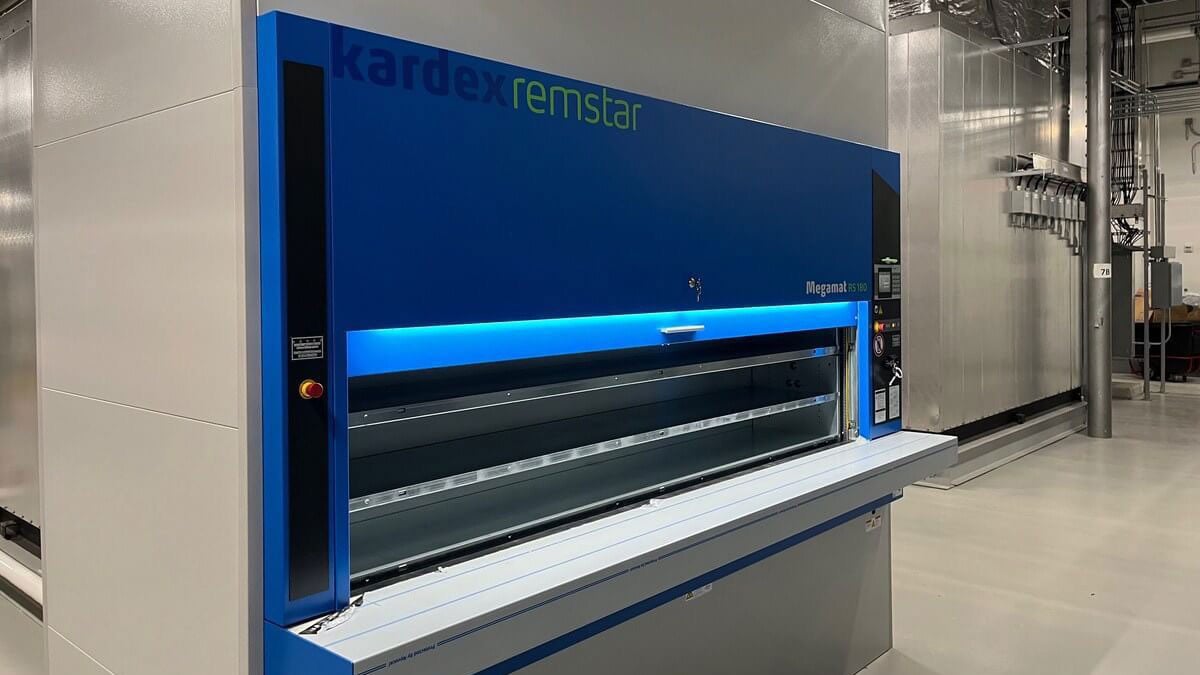 Unmanned Kardex Remstar Megamat RS 180 vertical storage carousel in an industrial setting with a closed access opening and stainless steel work surface