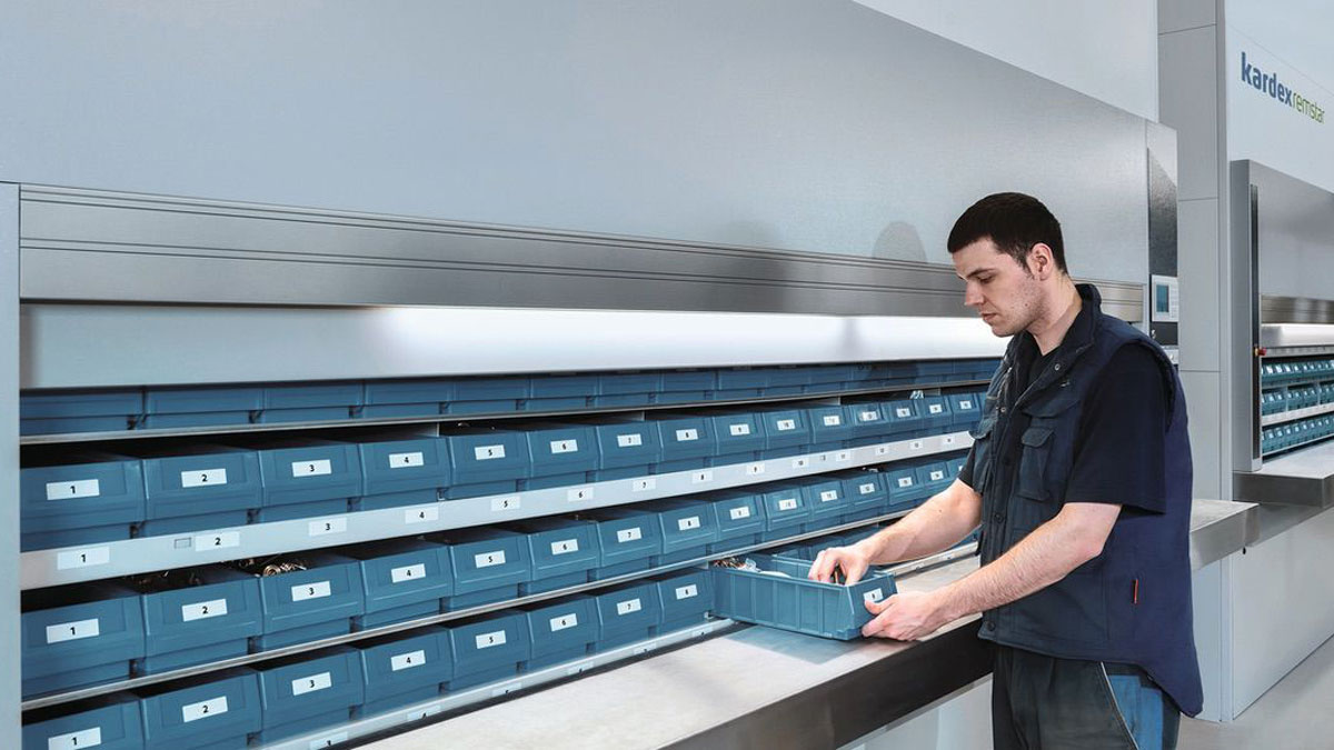 Warehouse employee retrieving a storage bin from a Kardex vertical carousel system, illustrating efficient small parts picking with labeled containers