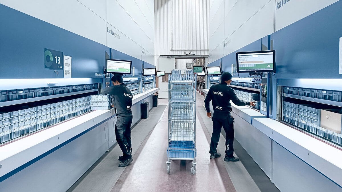 Workers using vertical carousels at logistics facility with inventory carts and integrated order-picking terminals for streamlined logistics