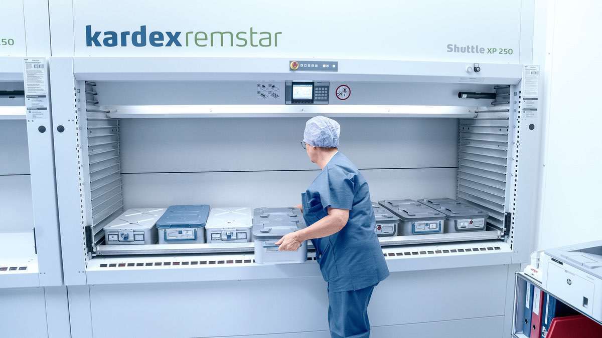 Clinician retrieving sterilized containers from a Kardex Shuttle XP VLM at a cleanroom pass-through