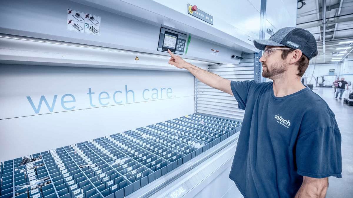 Warehouse worker operating a vertical lift module using a touchscreen interface to retrieve and manage inventory bins for streamlined order picking operations
