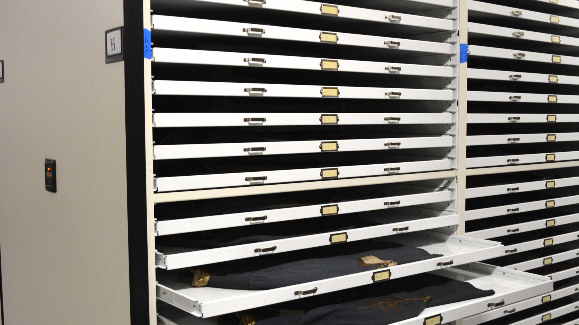 Pull-out flat-file drawers storing historic uniform textiles in museum archive cabinet.