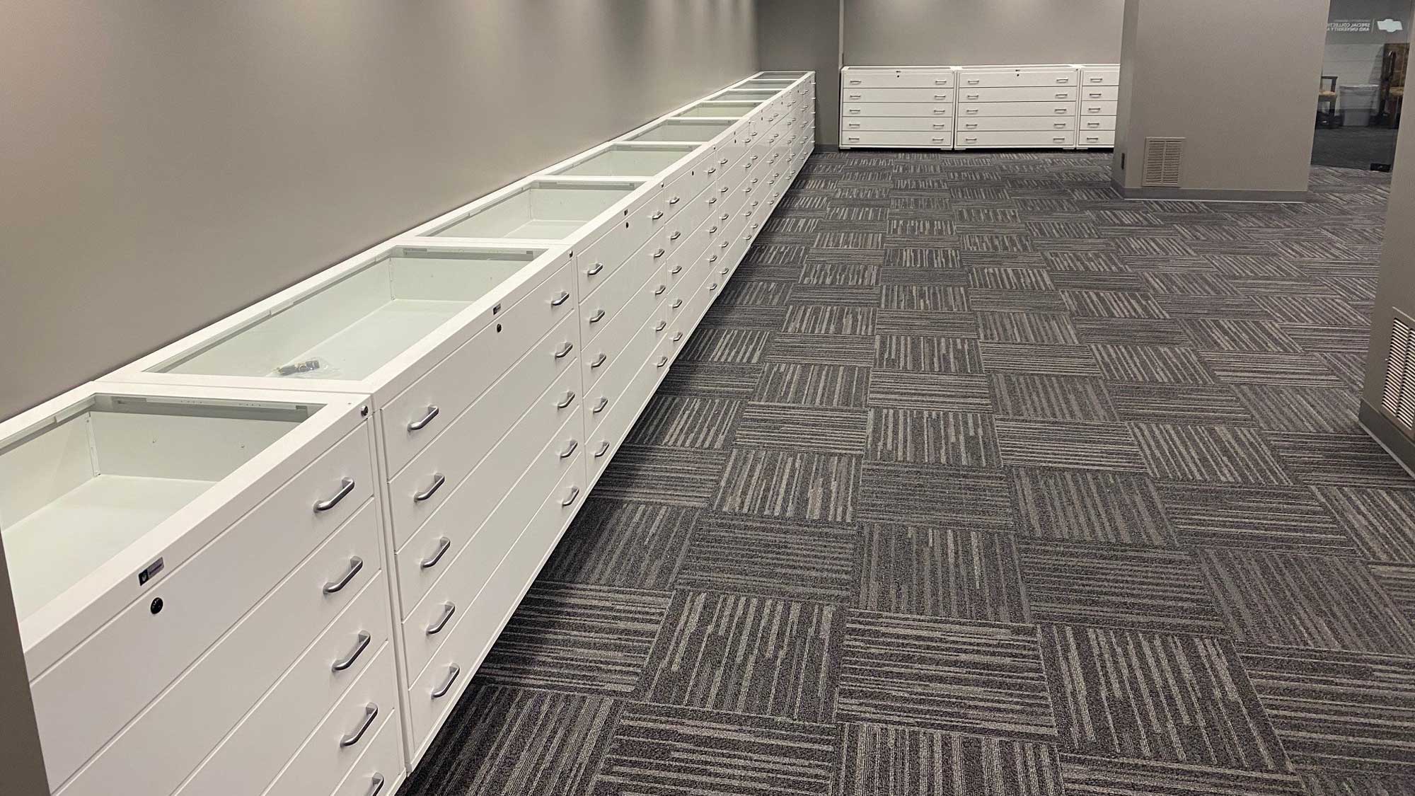 Flat-file cabinets with glass display lids and multiple drawers for map and document storage in a library setting
