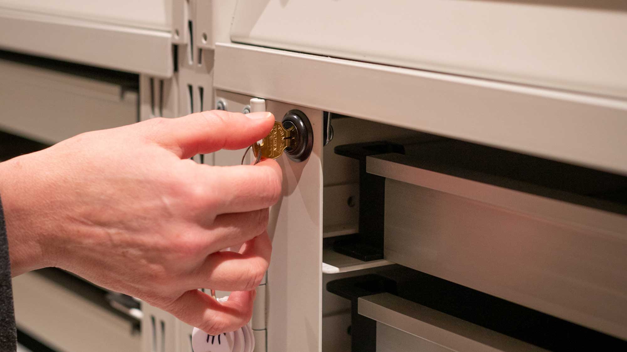 Close-up of a hand turning a key in the lock of a flat-file storage cabinet.