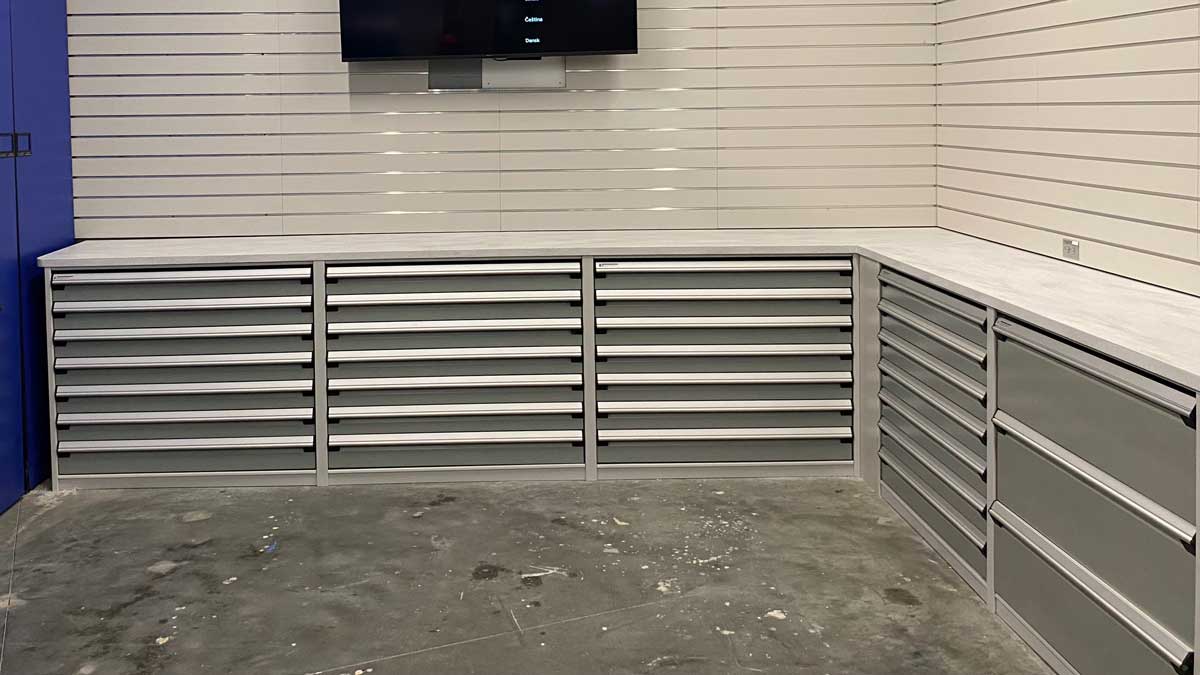 Row of tall dark grey drawer cabinets with open upper cubbies against a plain wall.