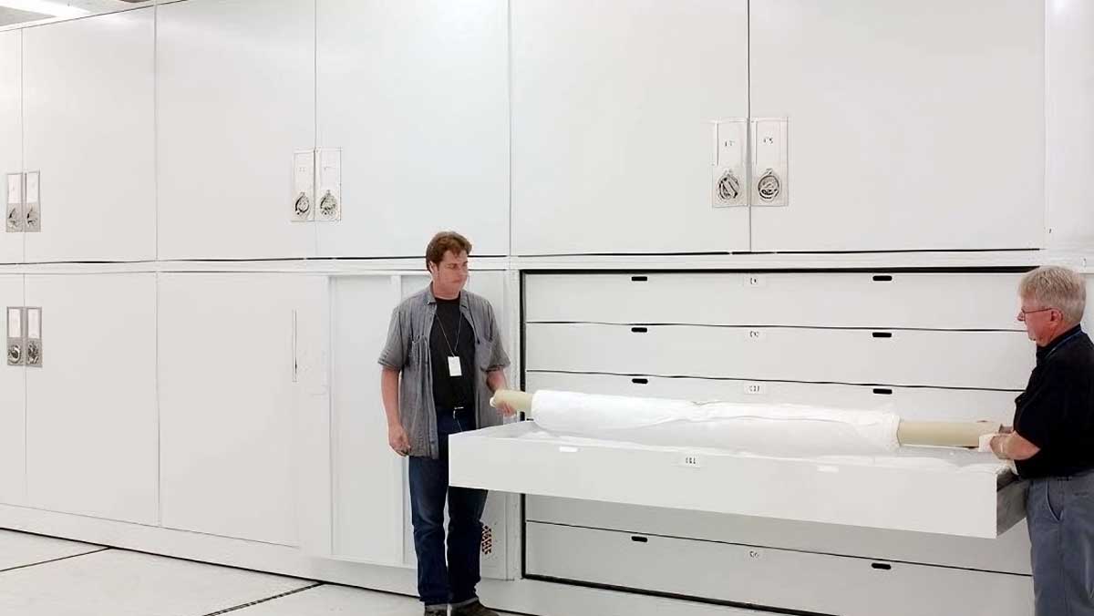 Museum staff managing a large white cabinet with wide pull-out drawers designed for delicate artifacts in a storage room