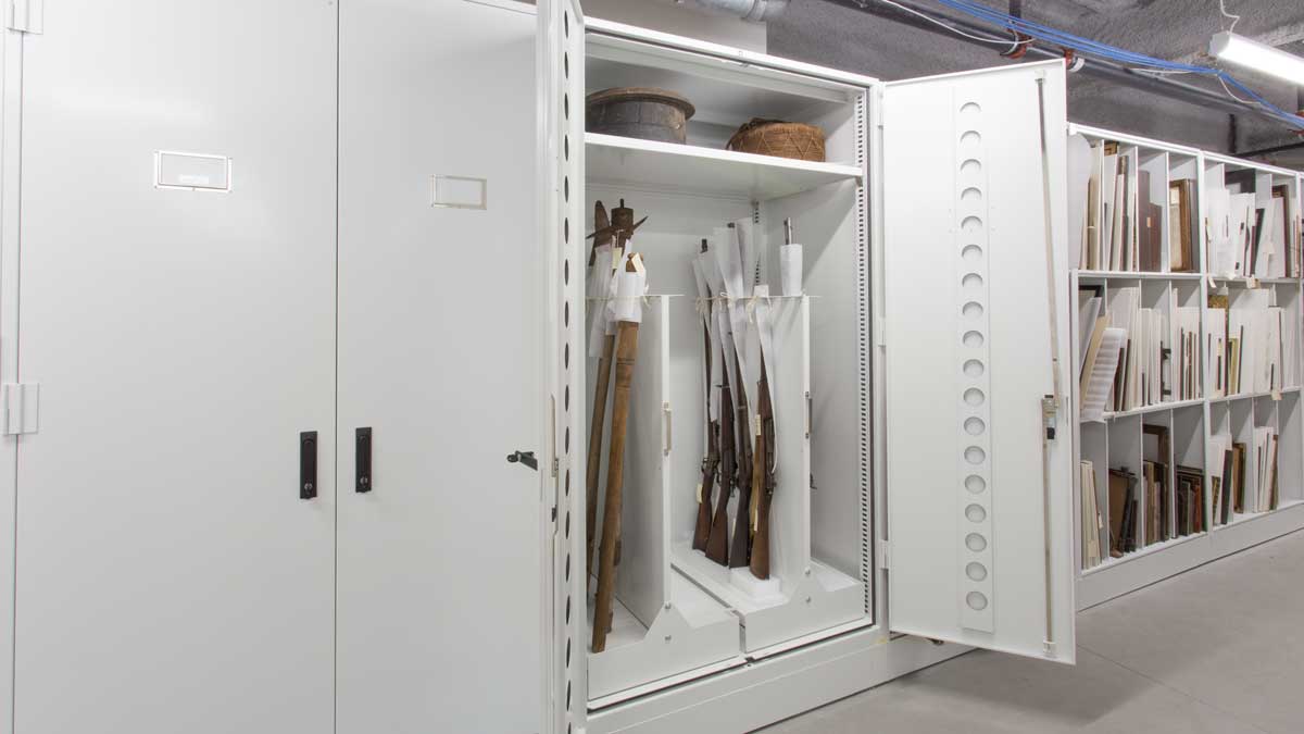 A white metal museum cabinet with a pull-out gun rack designed to store long rifles in an organized manner
