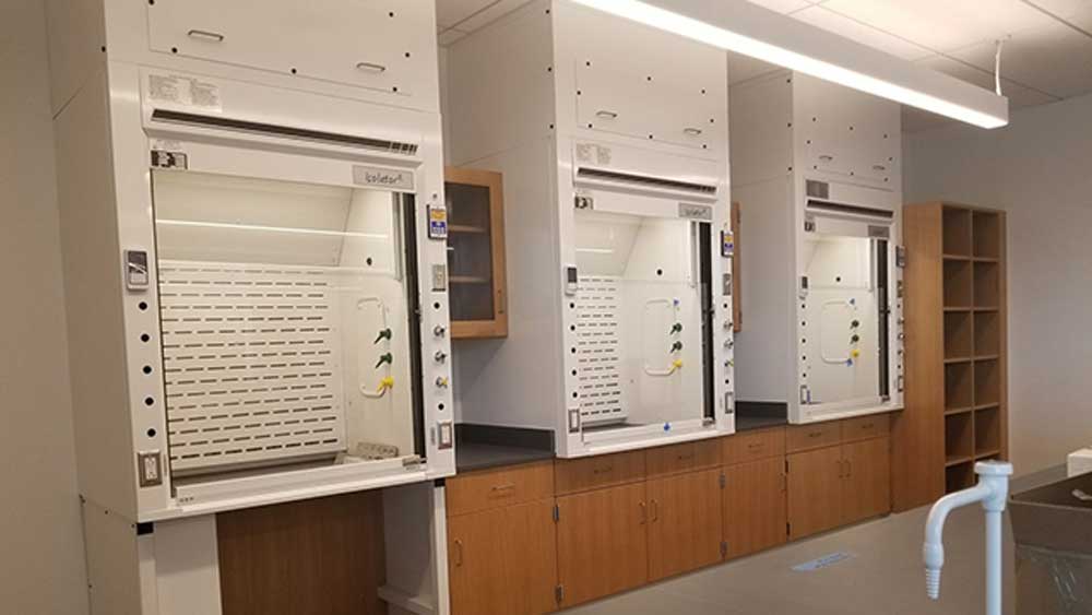 three built-in forensic laboratory fume hoods mounted above wood veneer base cabinets with glass sashes