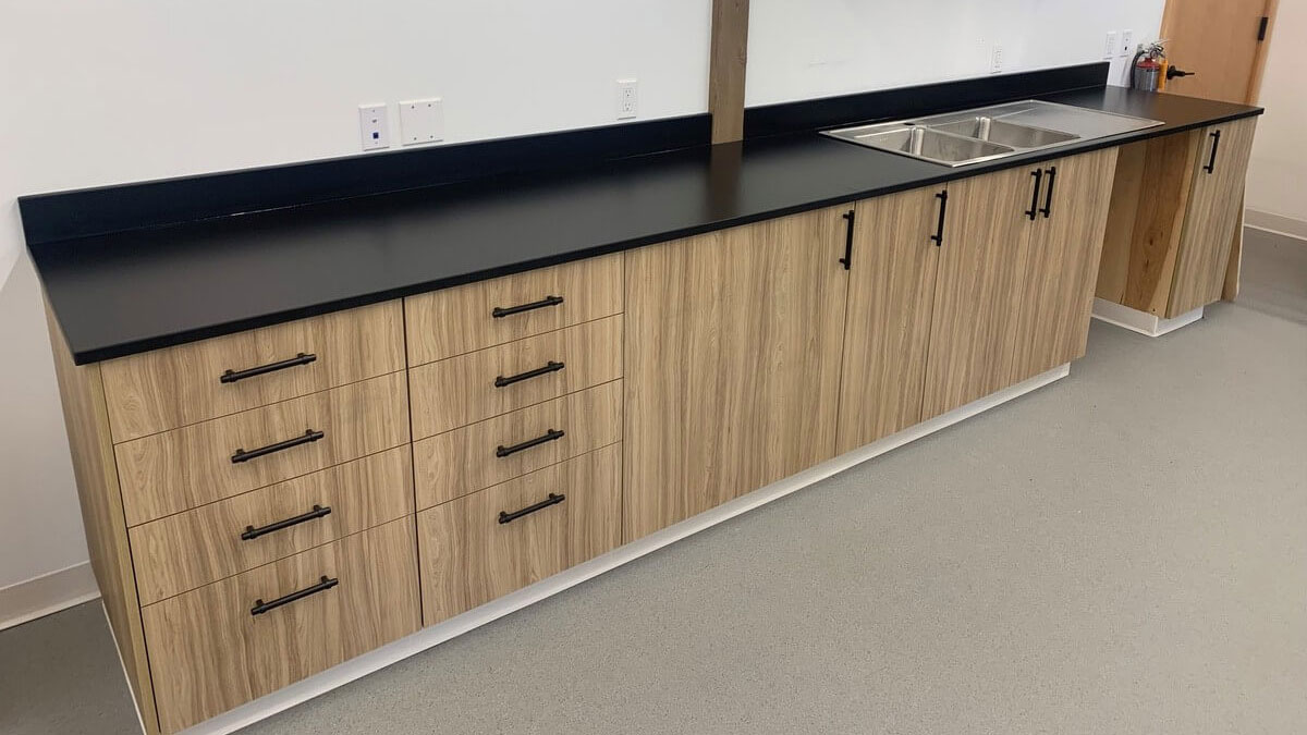 Woodgrain modular casework with black countertops and integrated sink in a commercial workspace.