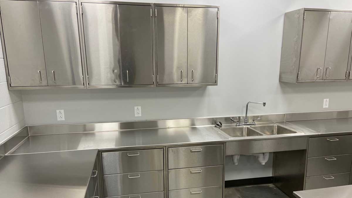 stainless steel casework in law enforcement setting with upper glass door cabinets and lower storage units