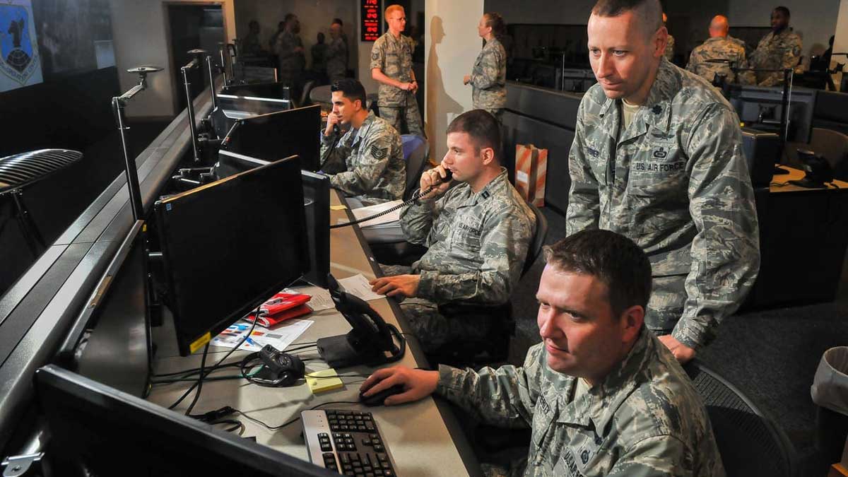 Military command center showing operators at control stations with multiple monitors and communication systems