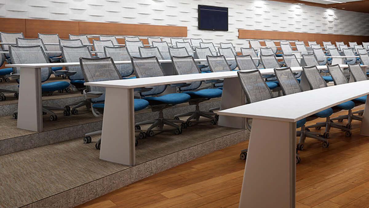 auditorium table setup with rows of mesh office chairs on casters arranged behind white tables in a tiered lecture room