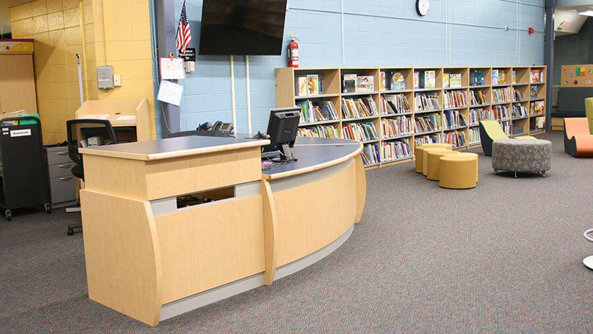 Maplebrook library circulation desk design with curved surfaces and integrated shelving for functional and welcoming service areas