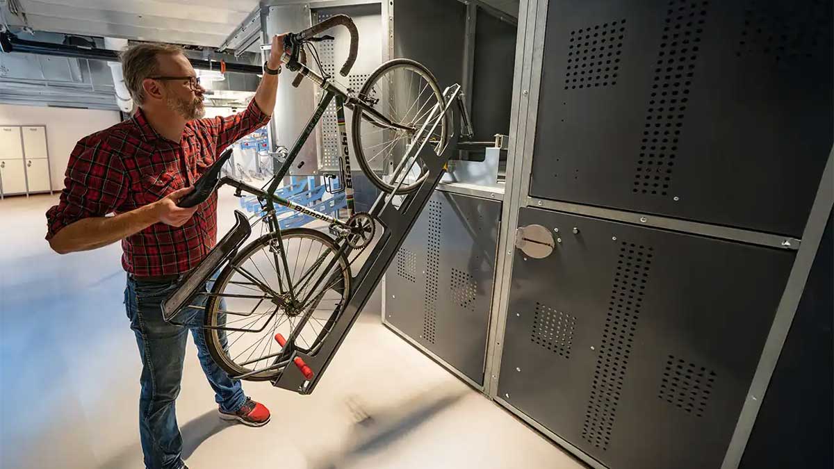 User loading bicycle into two‑tier bike locker
