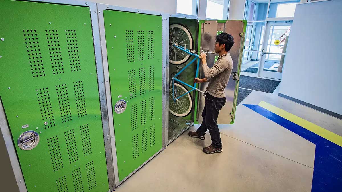 person loading bicycle into vertical bike locker storage compartment indoor