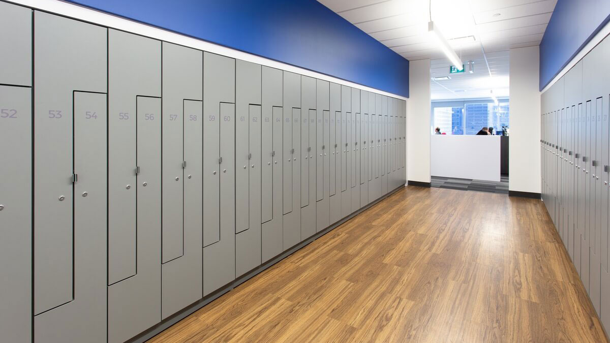 Gray numbered lockers in hallway with wood flooring and blue accent walls in modern office