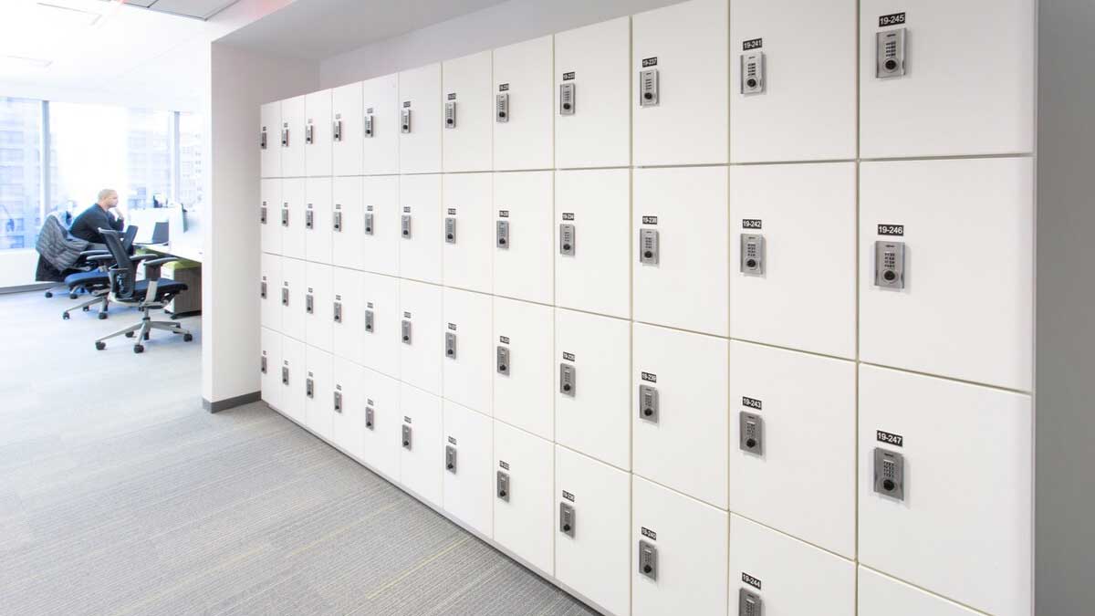 Wall of white lockers with keypad access in open office near workstation area