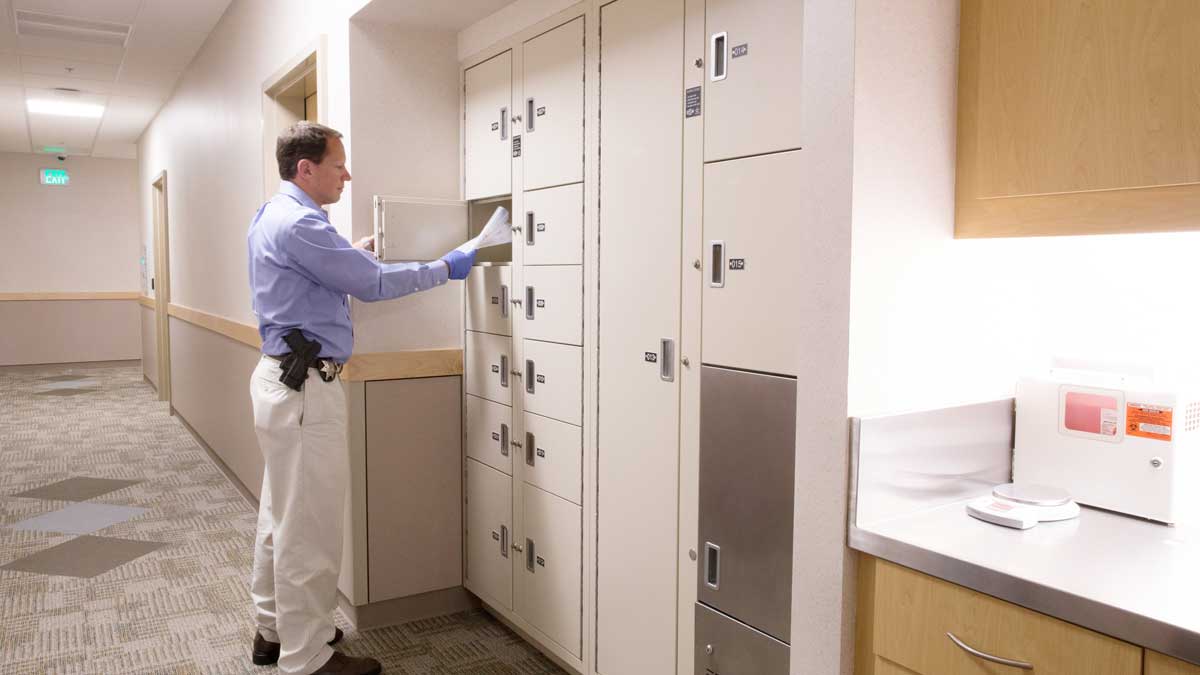 Police officer documenting items in front of temporary evidence storage lockers in secure room