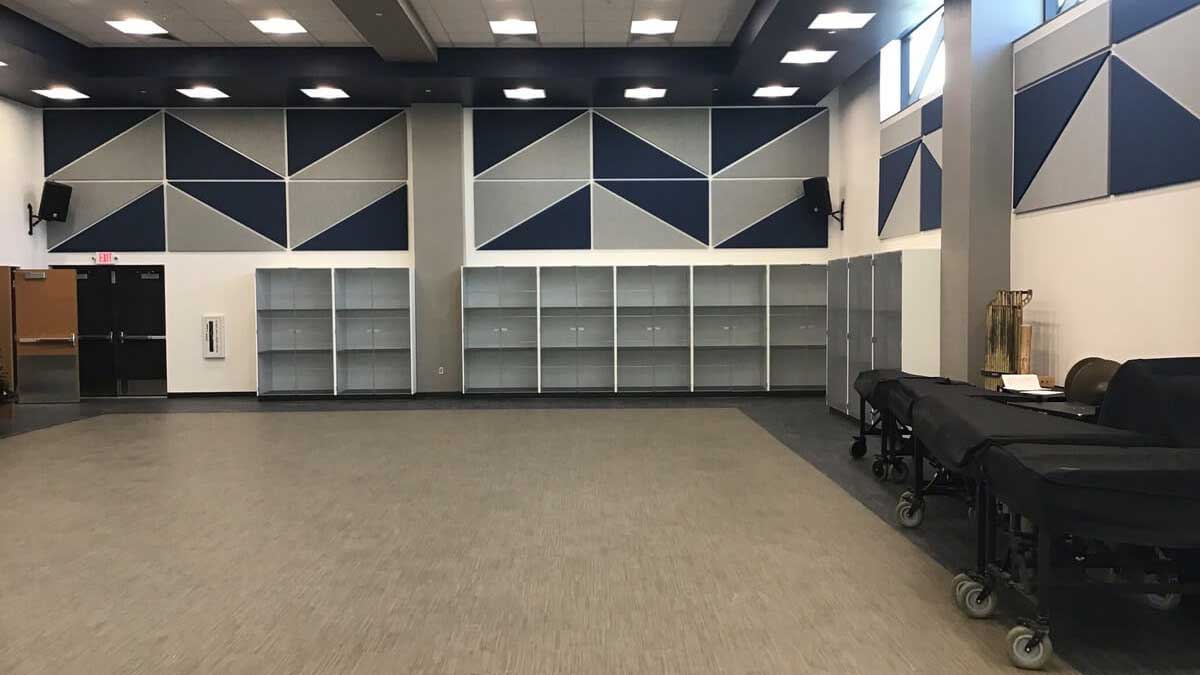 Empty instrument storage shelving in a modern band room with geometric wall paneling and high ceilings