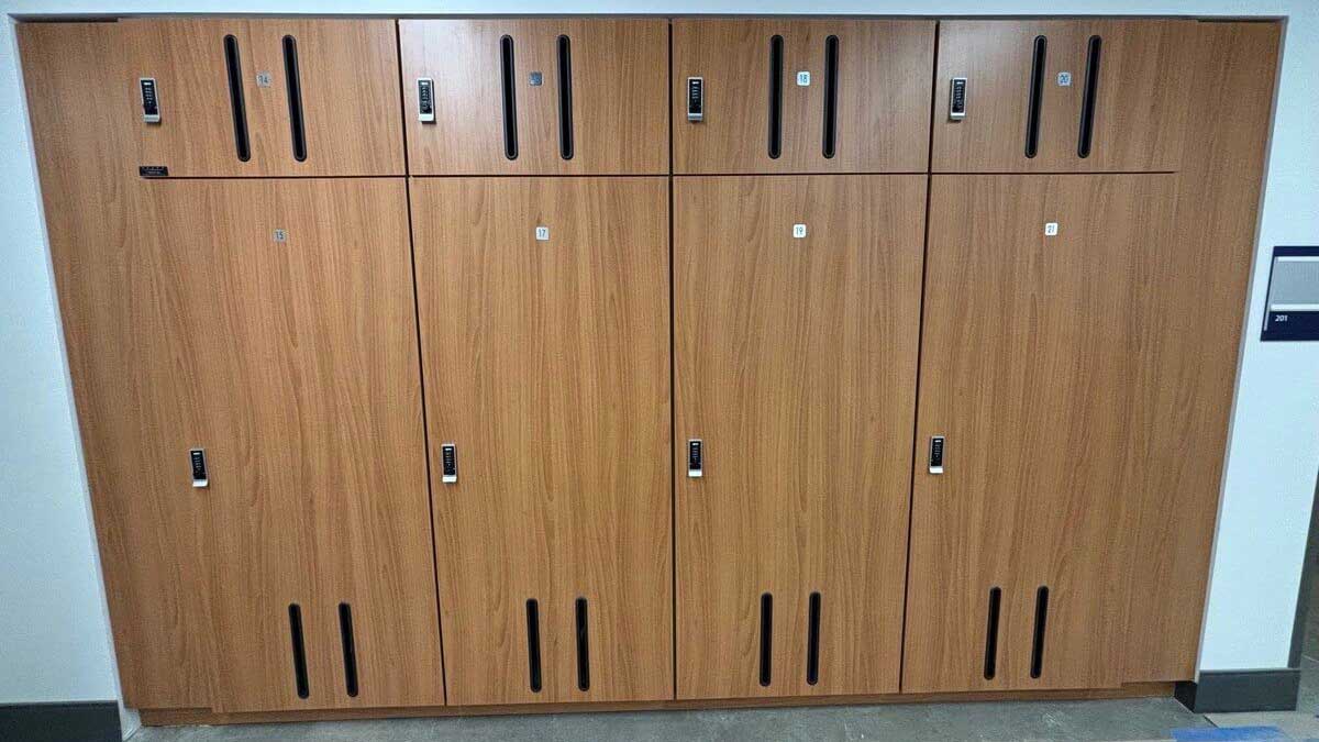 Oversized woodgrain instrument lockers with vent slots and keyless lock access for band equipment.