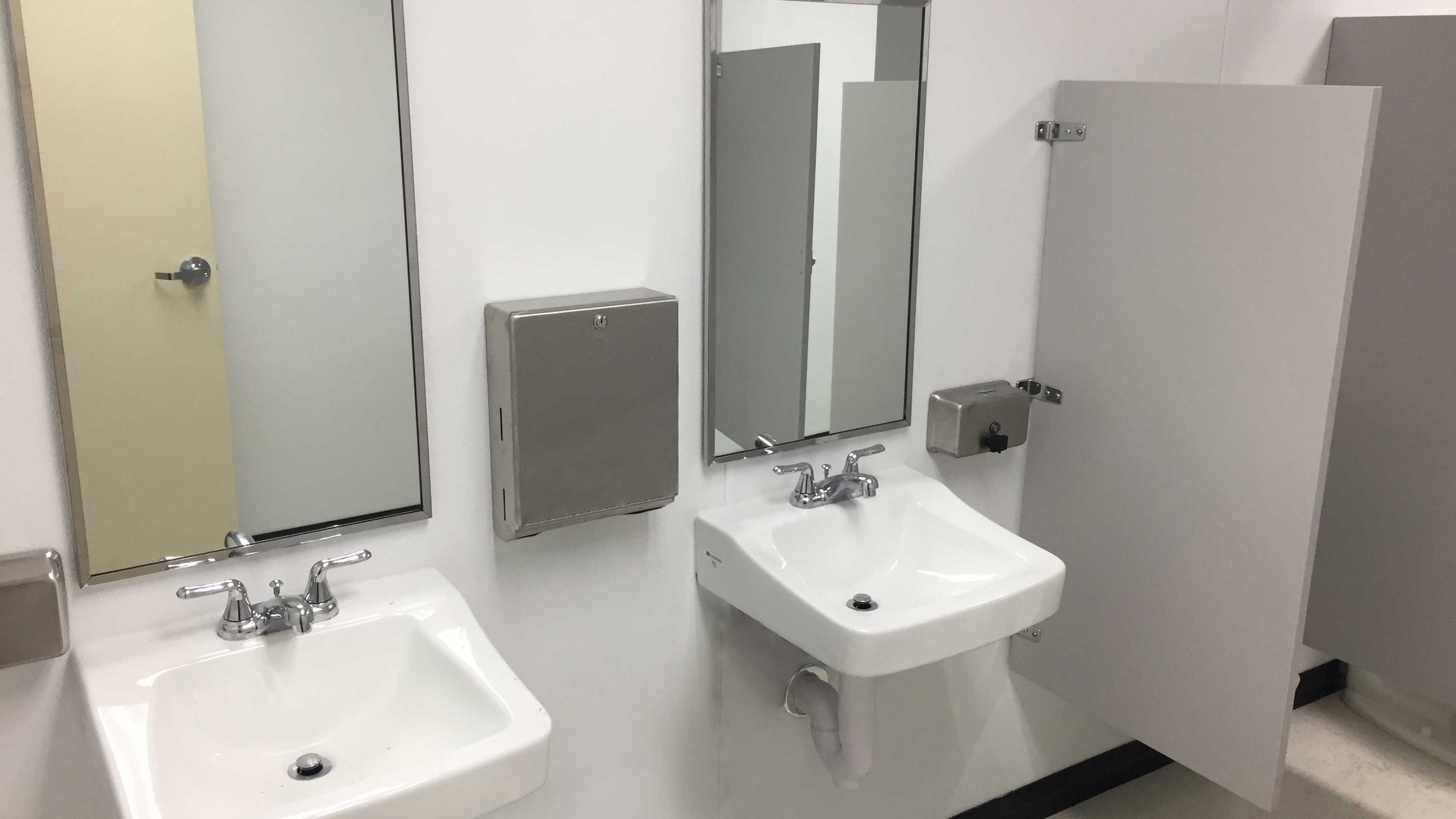 two wall-mounted bathroom sinks with mirrors and towel dispensers inside modular restroom pod