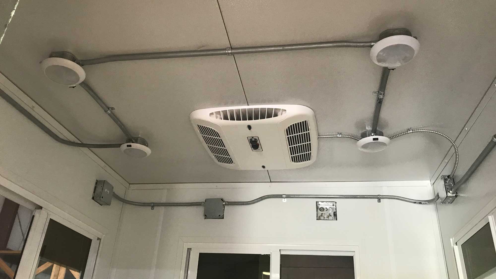 ceiling-mounted round light fixtures and air-conditioning unit installed in modular restroom pod