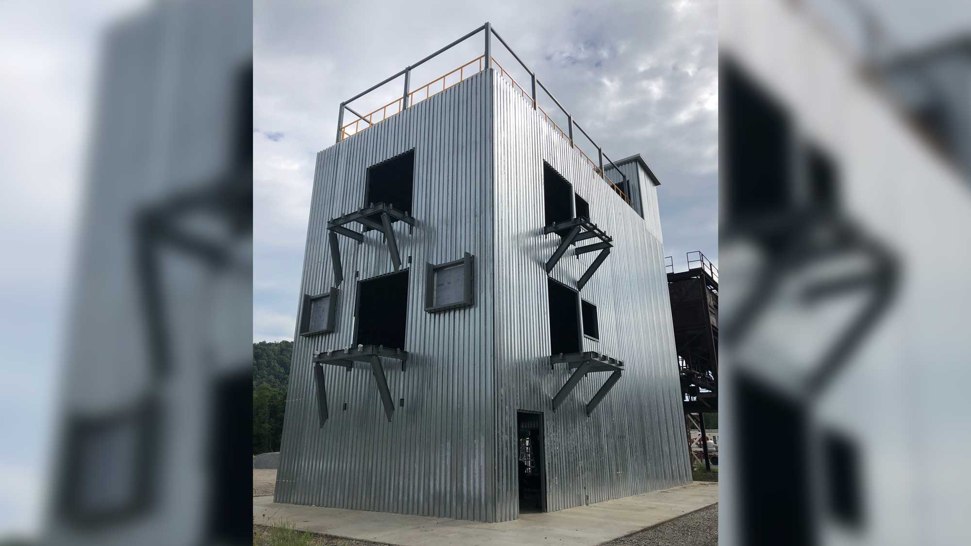 single-level elevated guard booth featuring a grey enclosed cabin, steel support columns and grated stairs in an outdoor setting