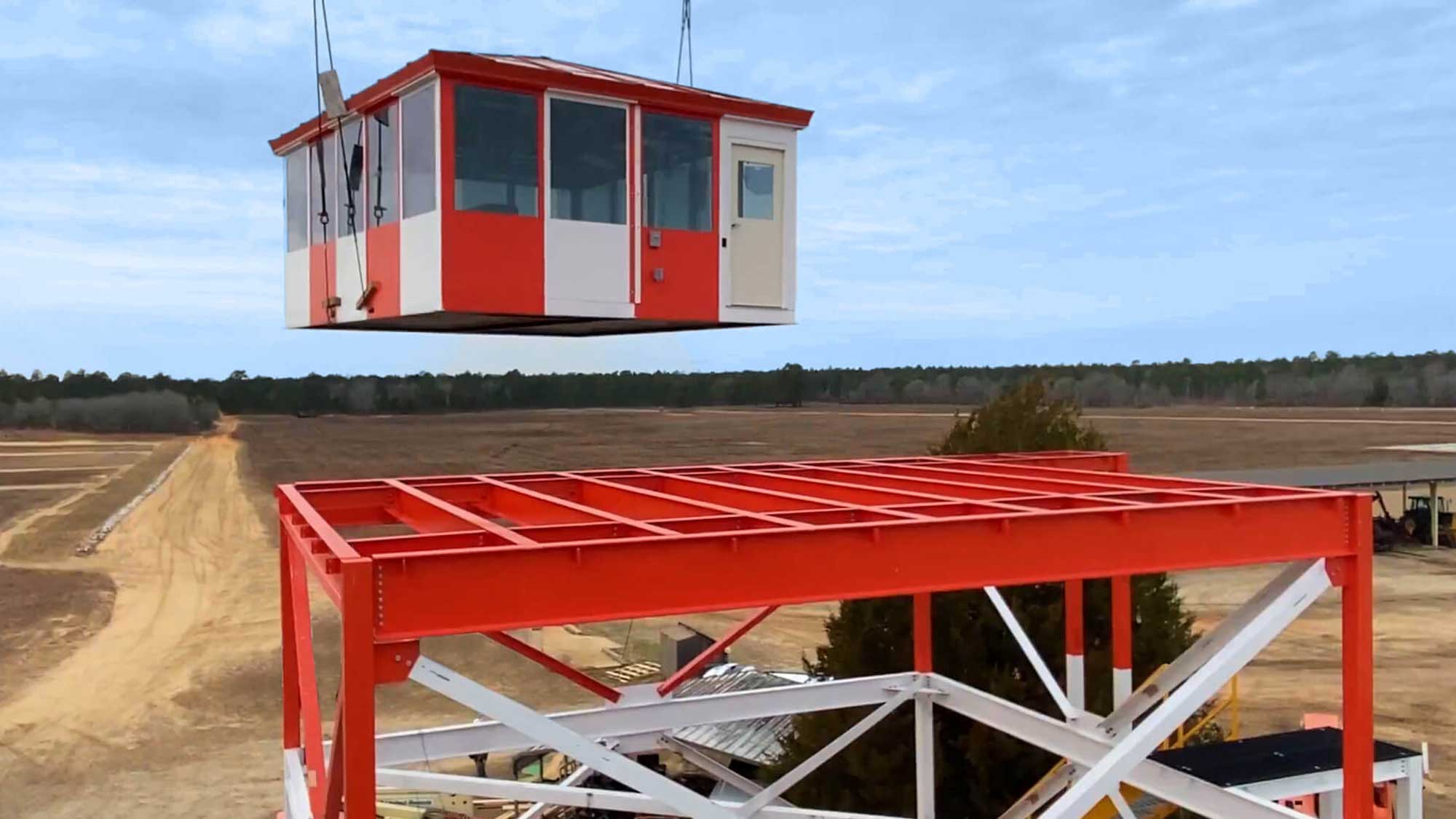 red and white modular guard cabin being lifted by crane onto an elevated steel tower frame at a remote site