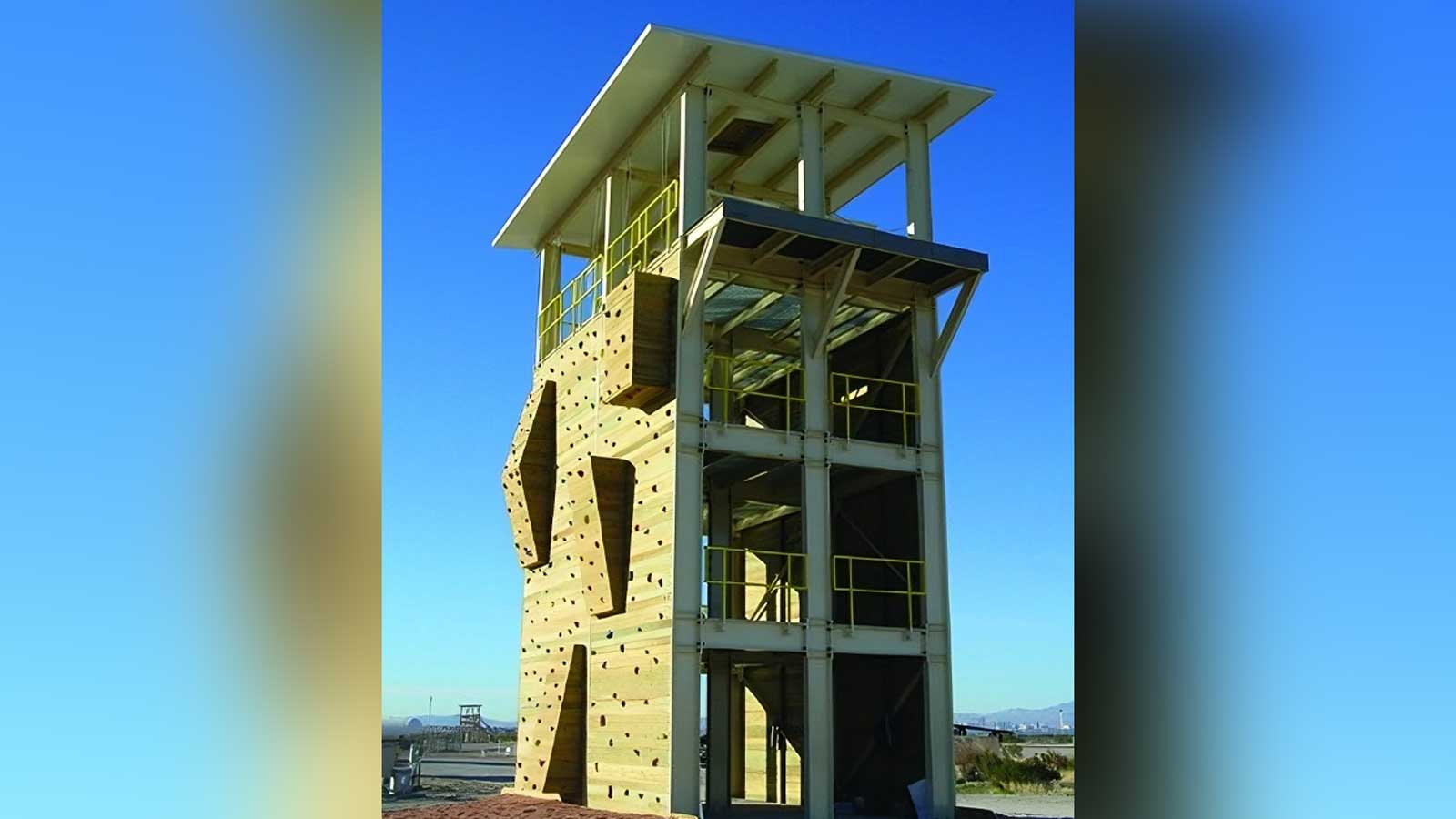 three-story steel training tower featuring integrated wood-panel climbing walls and open stair landings against a bright blue sky