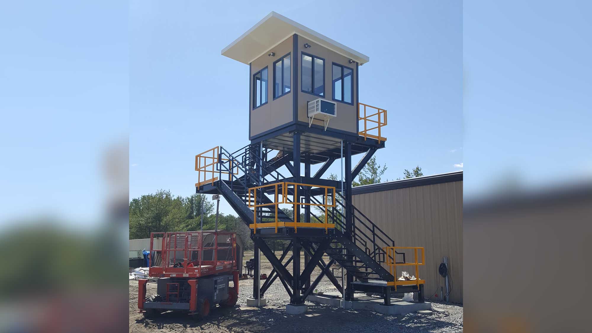 double-tier security tower with enclosed top cabin, wraparound platform and exterior staircases under clear blue sky