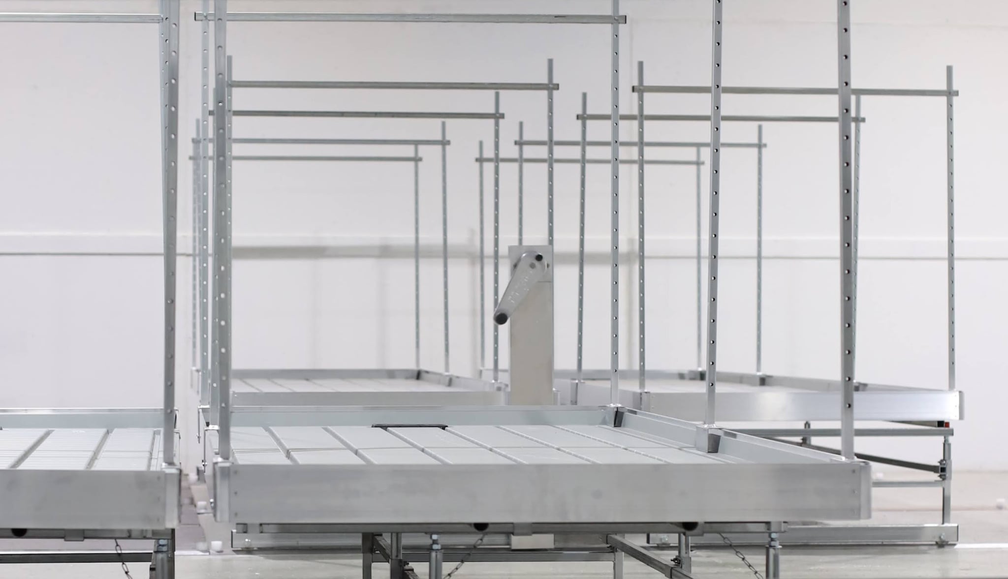 Tracked and rolling cannabis cultivation benches with white grow containers, healthy plants, and LED lighting in a controlled grow room.