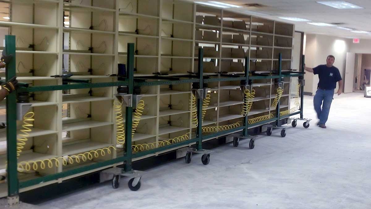 fully loaded library shelving units being relocated using wheeled track system for efficient facility reconfiguration