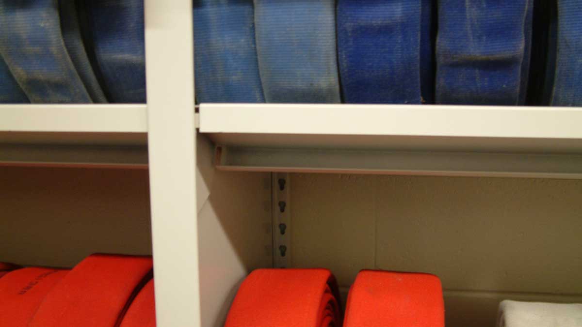 Close-up of heavy-duty steel shelving holding coiled blue and red fire hoses with their couplings facing outward.