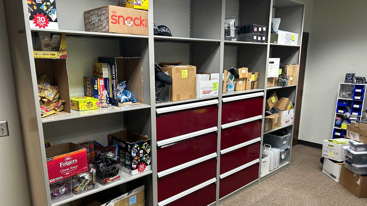 grey steel shelving with red drawers and open compartments holding office supplies and snacks