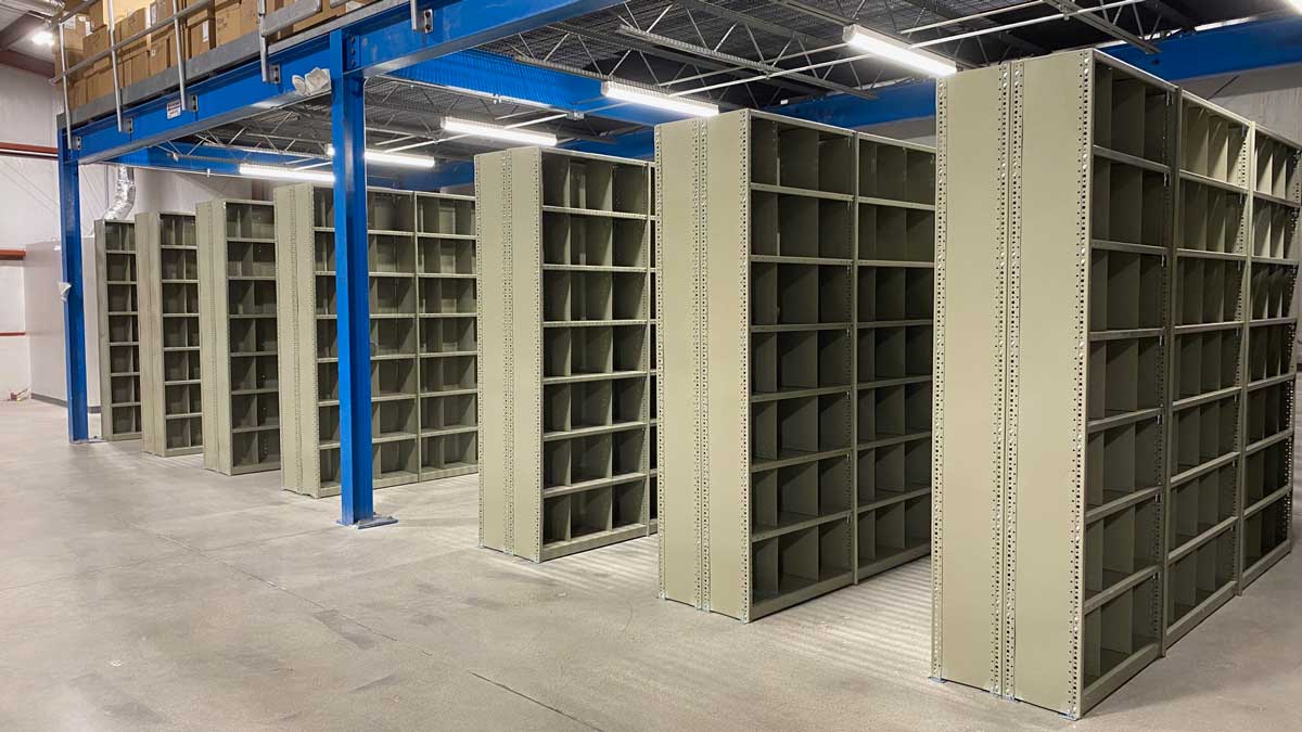 grey steel bin shelving units arranged in rows under overhead beams for small parts storage in warehouse