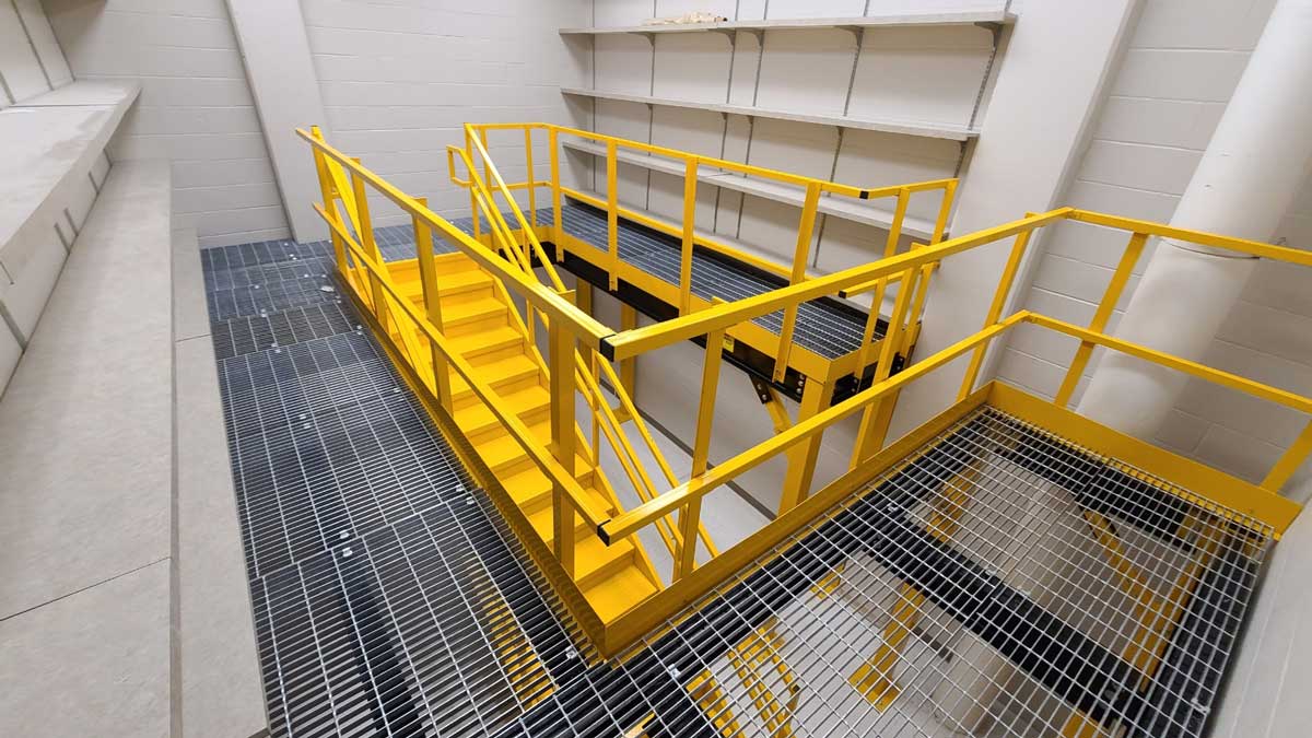 top-down view of a yellow safety-railed mezzanine platform with metal grated flooring and staircase in a storage room