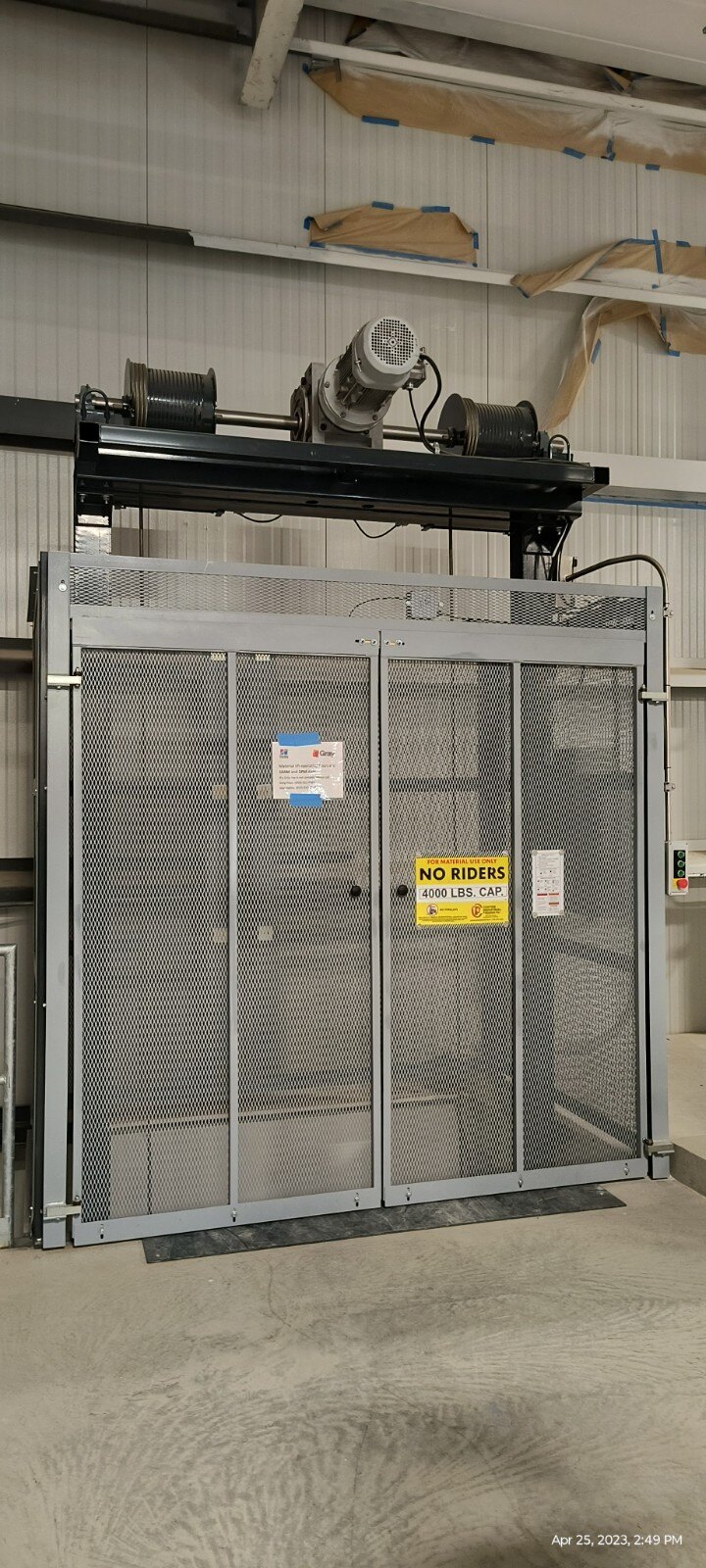 Industrial vertical material lift with mesh gate and 4000 lb capacity sign inside a warehouse facility