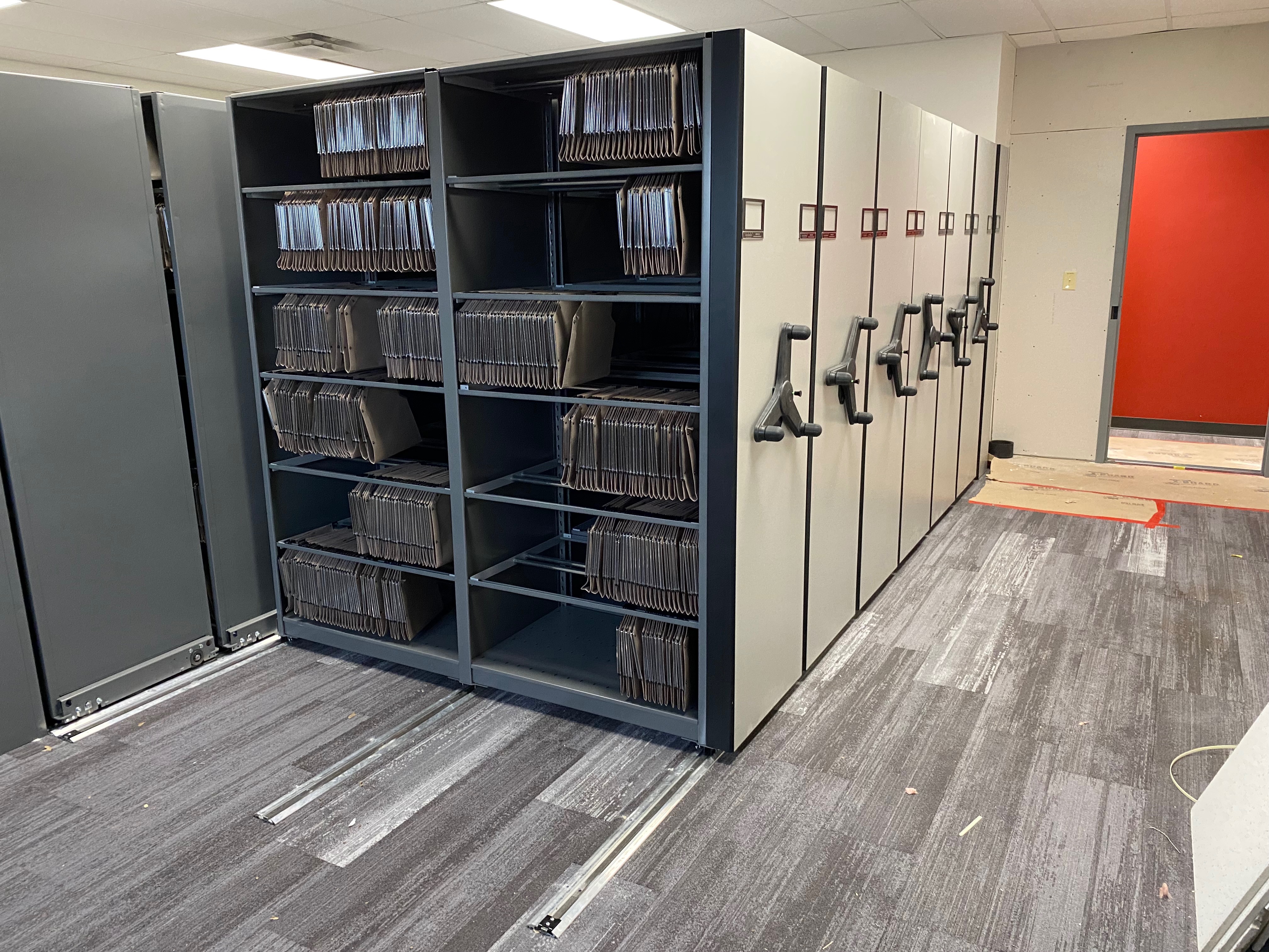 Oblique file storage system with side-tab folders and file folders with hooks hanging on rails in shelving.