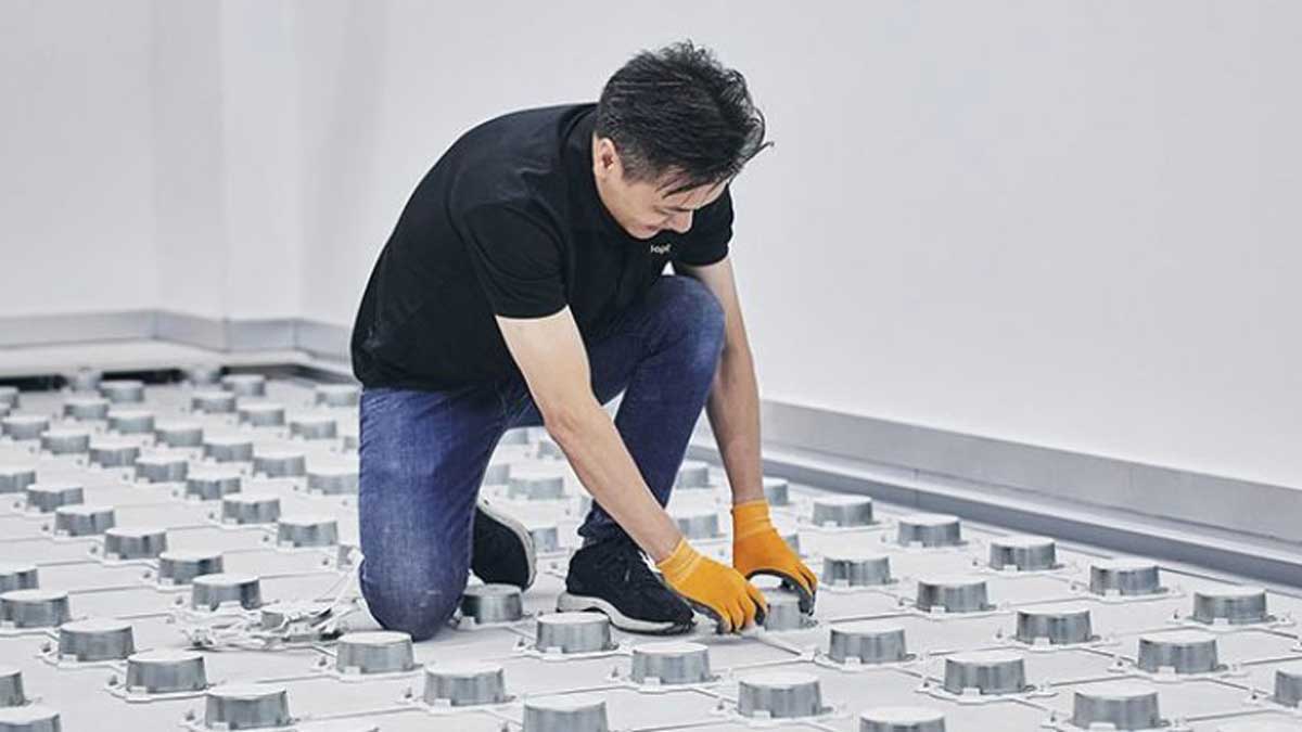 technician kneeling to secure pedestal base on raised access floor grid for panel support and leveling