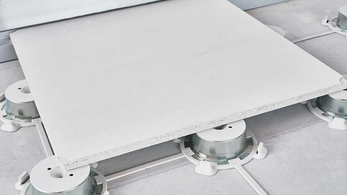 Close-up of a single concrete pedestal supporting a raised-floor panel, showing the precise interface between pedestal and tile. The smooth concrete floor beneath is visible around the edges.