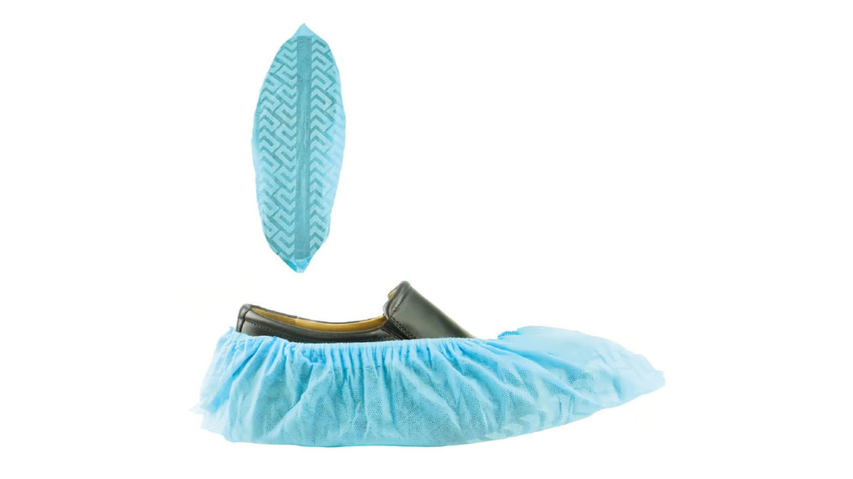 User applying shoe cover by pressing foot into dispenser slot