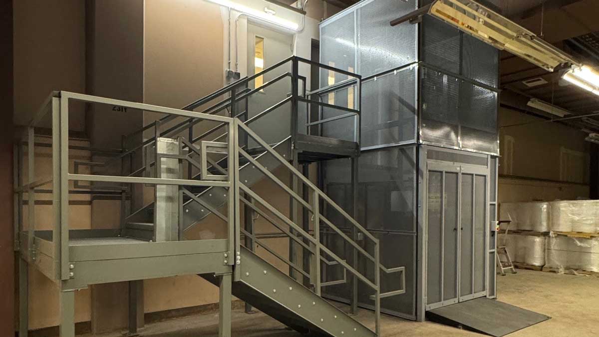 enclosed vertical material lift with adjacent stair access used for safe movement of goods between warehouse levels