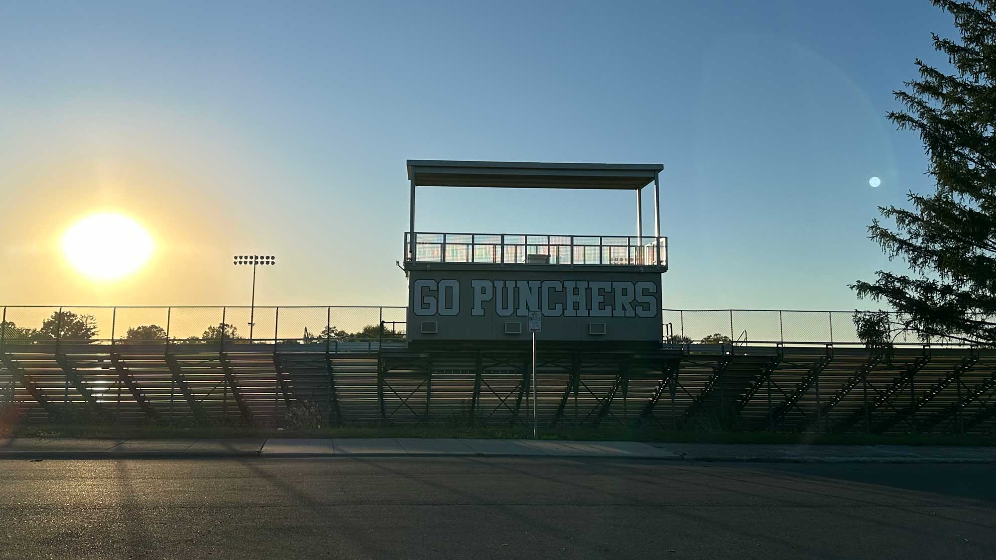 Press box mounted on bleachers with large team graphic and overhead camera deck