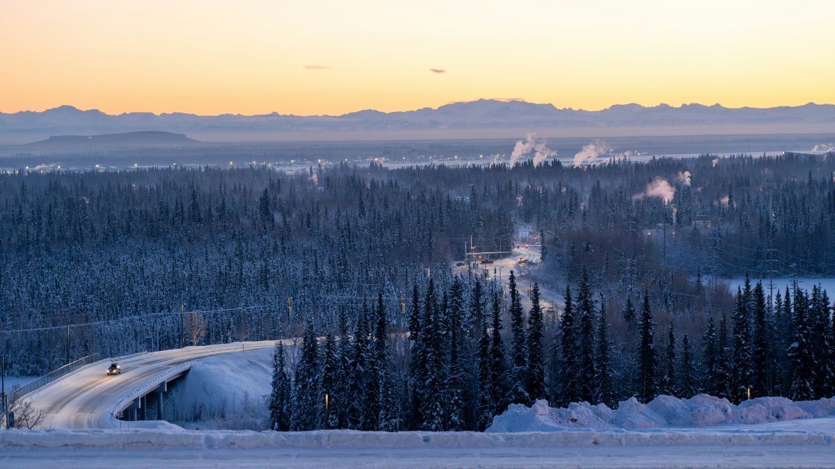 Winter view of Fairbanks with snow covered road, forest, and distant mountains